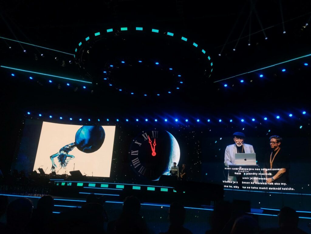 Nobelista fyzik Kip Thorne na festivale Starmus na pódiu číta básne o kozme, pri ňom stojí vizuálna umelkyňa Lia Halloran, ktorej ilustrácie sa premietajú na druhej strane pódia.