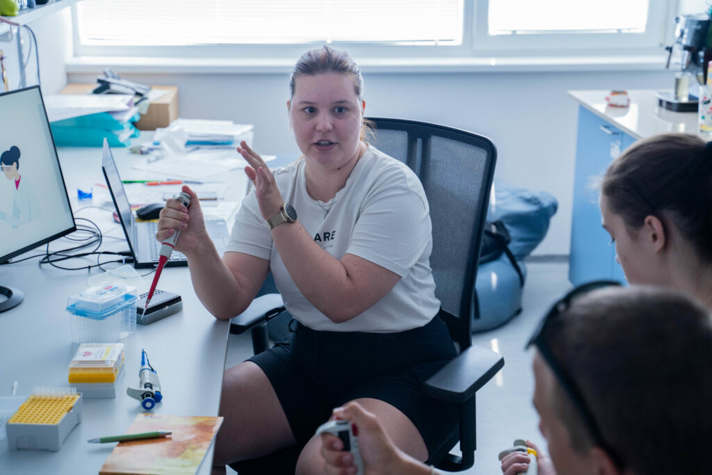 Letná škola mladých vedcov 2024, vedkyňa vysvetľuje prácu s pipetou.